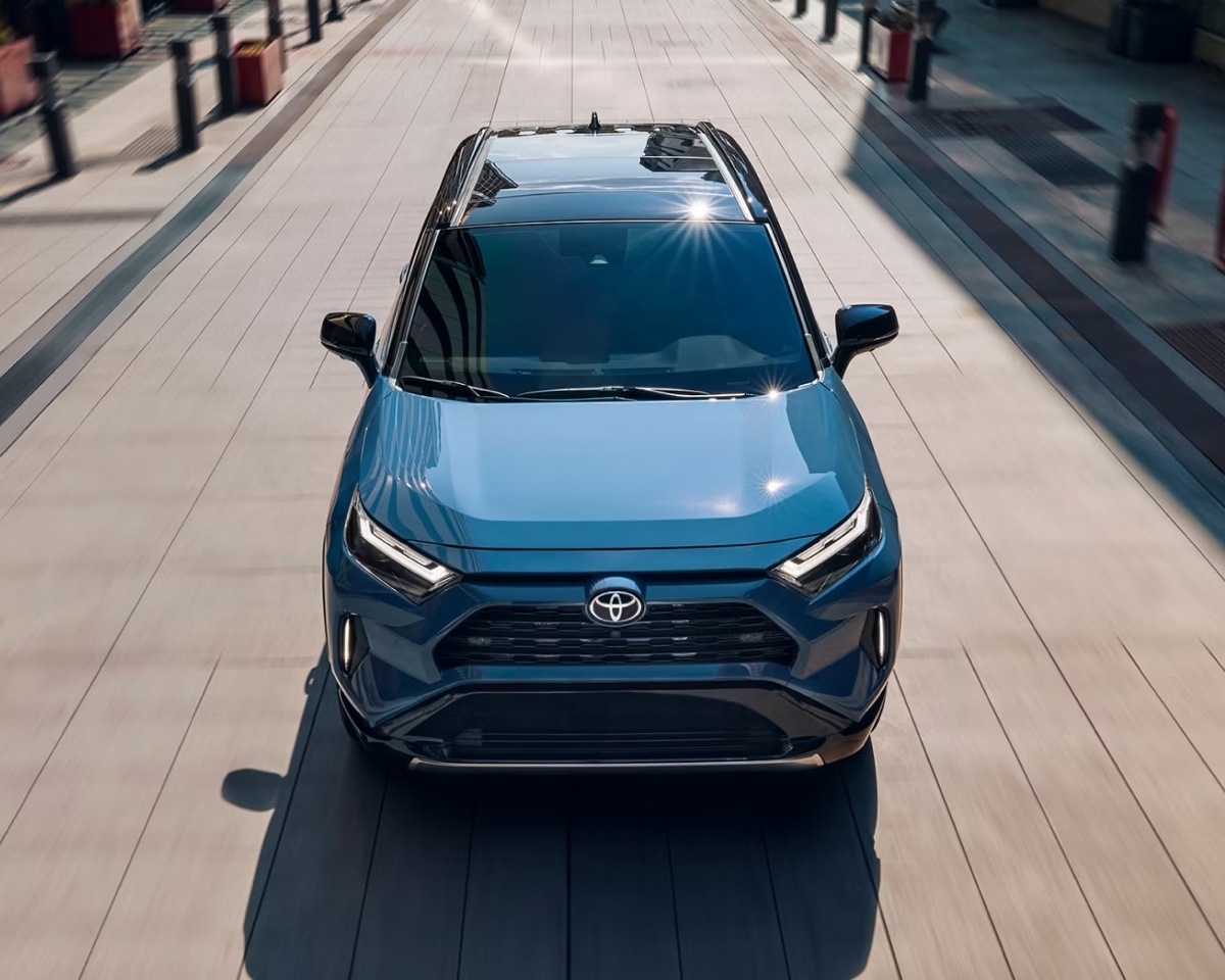 Vue frontale du Toyota RAV4 hybride bleu stationné en pleine lumière dans une allée moderne, montrant le design audacieux de la calandre.