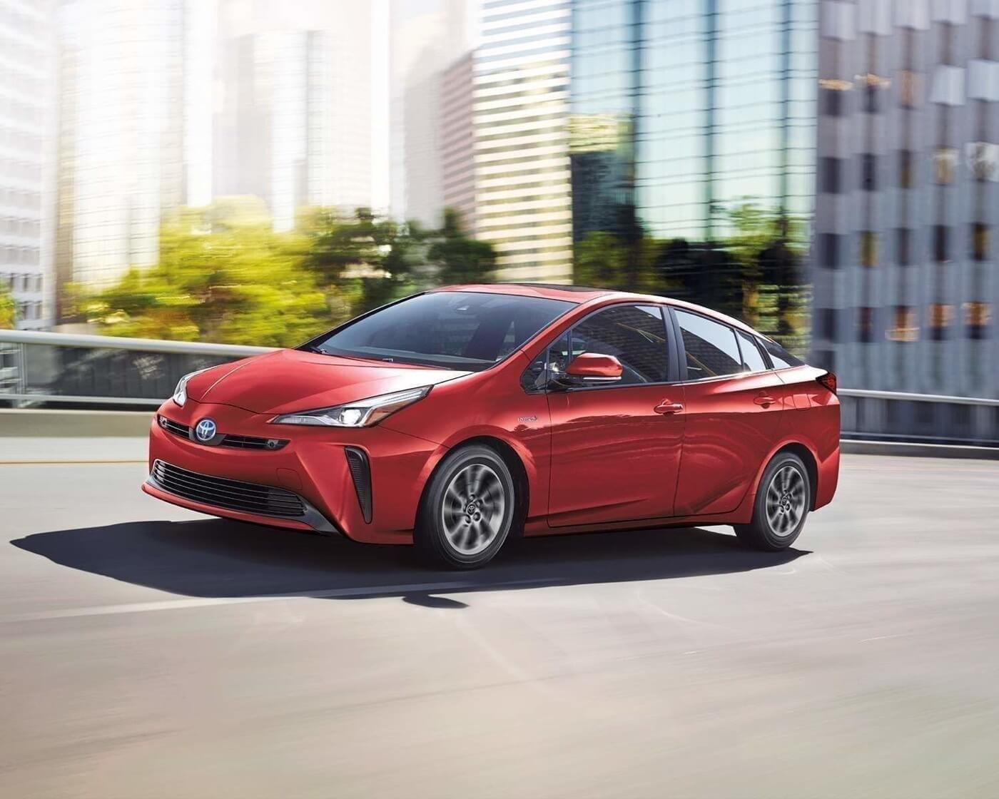 Toyota Prius hybride rouge 2022 en conduite urbaine, voiture d’occasion fiable et économique.