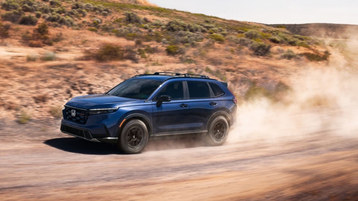 Honda CR-V hybride 2026 bleu foncé roulant sur un chemin de terre désertique, soulevant de la poussière, illustrant ses capacités hors route.
